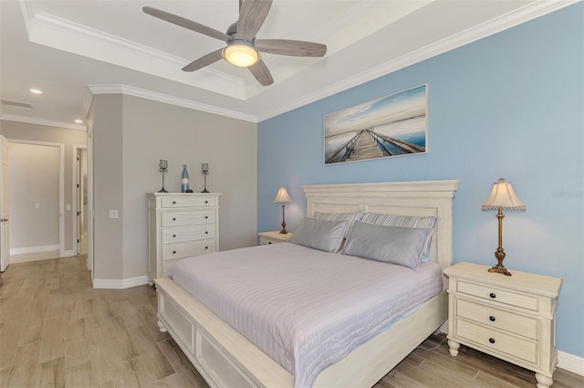 bedroom with a tray ceiling, ornamental molding, ceiling fan, and light wood-type flooring