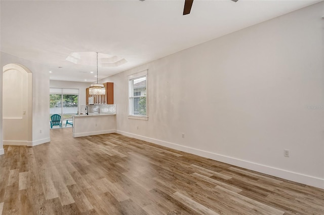 unfurnished living room featuring ceiling fan with notable chandelier and light wood-type flooring