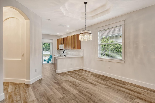 kitchen featuring a raised ceiling, kitchen peninsula, light hardwood / wood-style floors, and hanging light fixtures