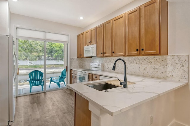 kitchen featuring light stone counters, white appliances, kitchen peninsula, and sink