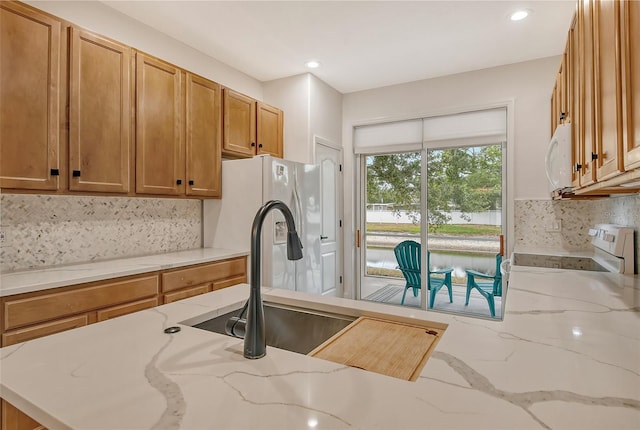 kitchen featuring light stone countertops, sink, decorative backsplash, and stove