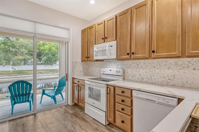 kitchen featuring light stone counters, white appliances, light hardwood / wood-style flooring, and backsplash