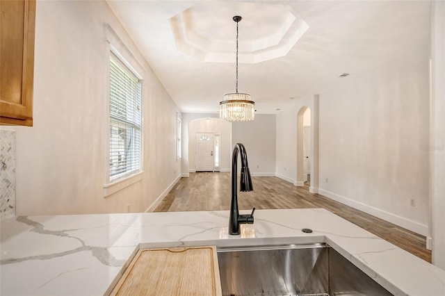 kitchen with sink, hanging light fixtures, a tray ceiling, light stone countertops, and light wood-type flooring