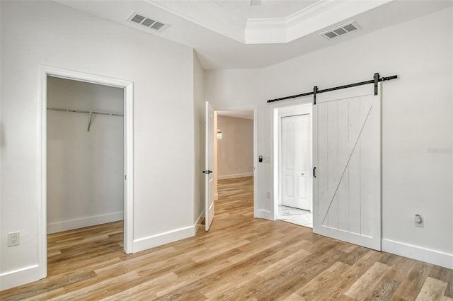 unfurnished bedroom featuring a closet, ornamental molding, a barn door, and light wood-type flooring