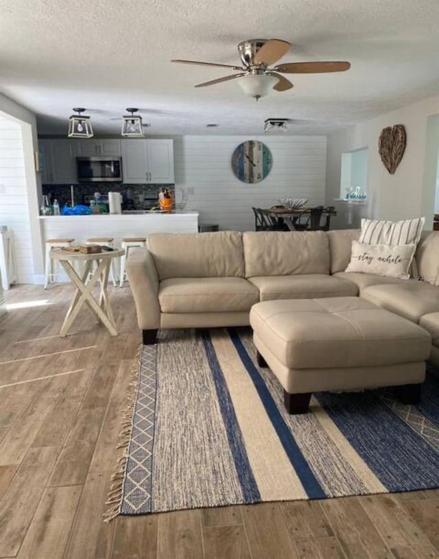 living room featuring hardwood / wood-style flooring, ceiling fan, and a textured ceiling