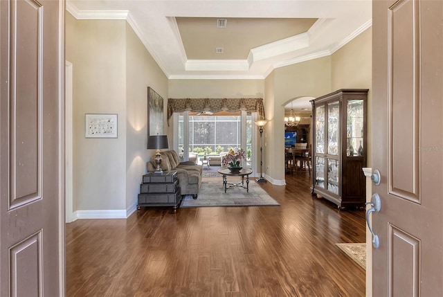 foyer featuring dark wood-type flooring, a tray ceiling, crown molding, and a notable chandelier