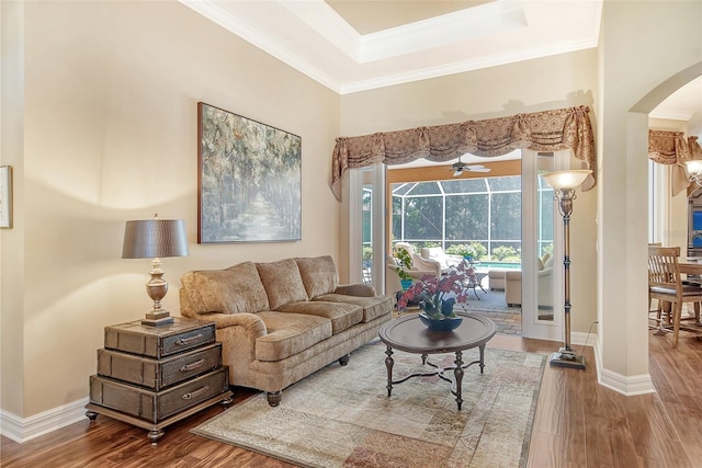 living room with a raised ceiling, wood-type flooring, and crown molding