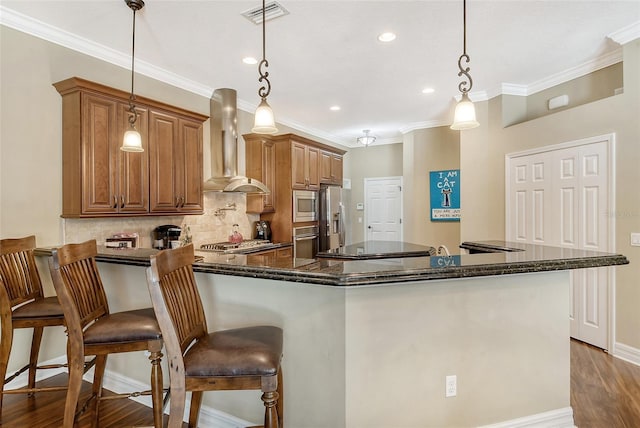 kitchen featuring appliances with stainless steel finishes, hanging light fixtures, wood-type flooring, a kitchen bar, and exhaust hood