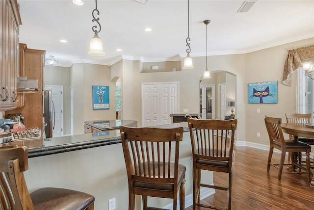 kitchen with dark wood-type flooring, stainless steel refrigerator, a breakfast bar, ventilation hood, and decorative light fixtures