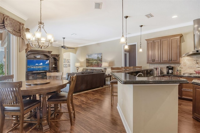 kitchen with crown molding, decorative light fixtures, dark hardwood / wood-style floors, a kitchen breakfast bar, and wall chimney range hood