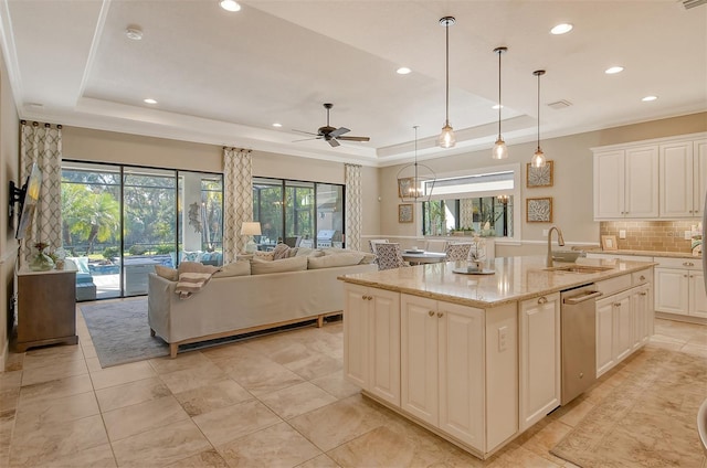 kitchen with an island with sink, sink, hanging light fixtures, a raised ceiling, and light stone countertops