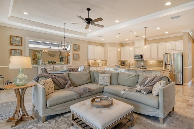 living room with light tile patterned flooring, ornamental molding, ceiling fan with notable chandelier, and a tray ceiling