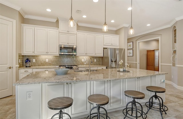 kitchen featuring a breakfast bar, hanging light fixtures, stainless steel appliances, an island with sink, and white cabinets