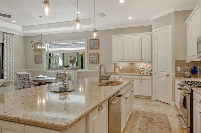 kitchen with stainless steel appliances, an island with sink, a raised ceiling, and sink