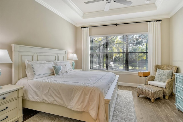 bedroom with ceiling fan, ornamental molding, a tray ceiling, and light wood-type flooring