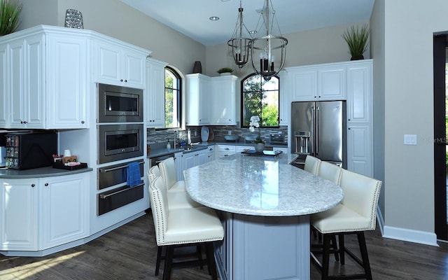 kitchen with a center island, hanging light fixtures, stainless steel appliances, decorative backsplash, and white cabinets