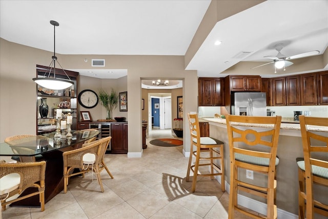 kitchen with a kitchen bar, stainless steel fridge with ice dispenser, light tile patterned floors, pendant lighting, and ceiling fan with notable chandelier