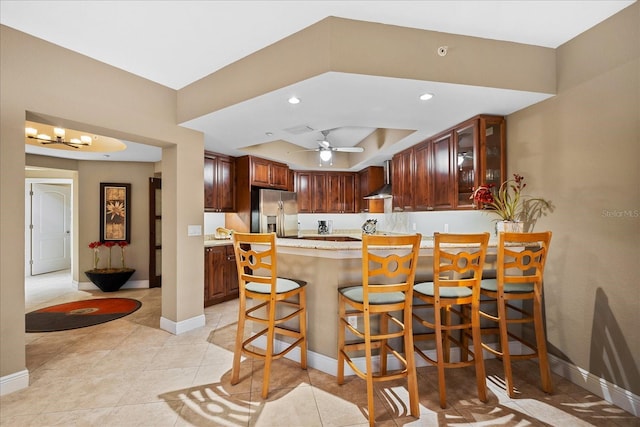 kitchen featuring stainless steel fridge with ice dispenser, kitchen peninsula, a breakfast bar area, ceiling fan, and a tray ceiling