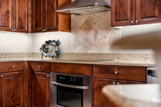 kitchen featuring backsplash, stainless steel oven, light stone countertops, and exhaust hood