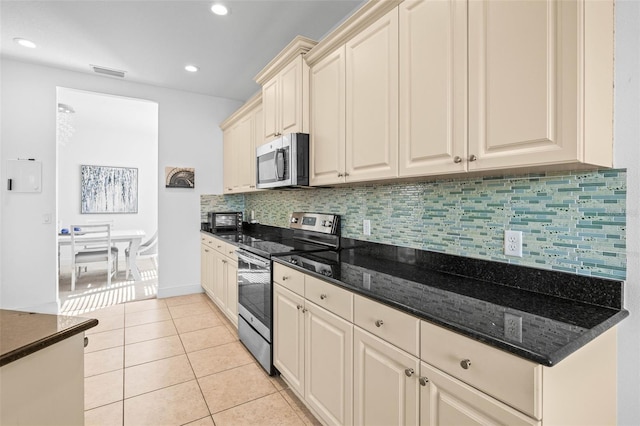 kitchen with light tile patterned floors, dark stone countertops, stainless steel appliances, decorative backsplash, and cream cabinetry