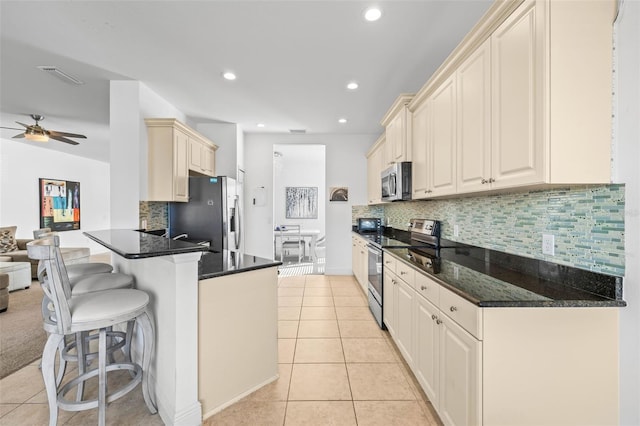 kitchen with dark stone countertops, light tile patterned flooring, kitchen peninsula, and appliances with stainless steel finishes