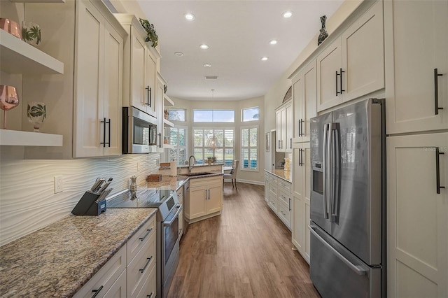 kitchen featuring sink, decorative backsplash, hardwood / wood-style flooring, light stone counters, and stainless steel appliances