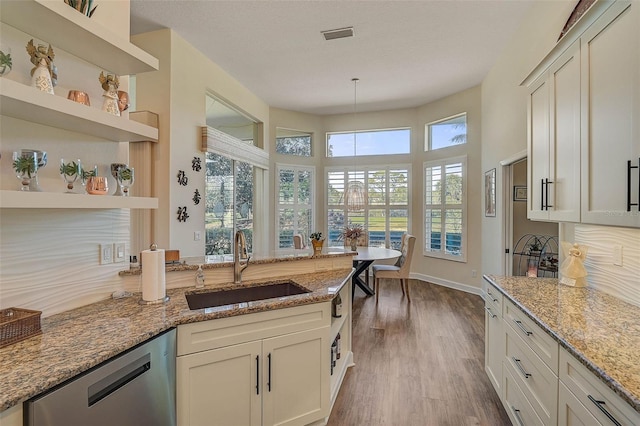 kitchen with sink, dark wood-type flooring, dishwasher, hanging light fixtures, and light stone counters