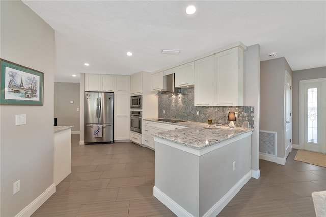 kitchen with stainless steel appliances, light stone countertops, wall chimney range hood, decorative backsplash, and white cabinetry