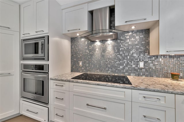 kitchen with exhaust hood, stainless steel appliances, light stone counters, decorative backsplash, and white cabinetry