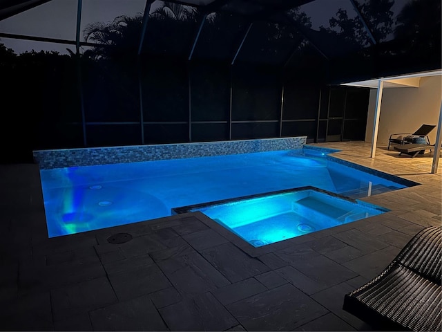 pool at night with a patio area, an in ground hot tub, and a lanai