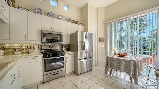 kitchen with light tile patterned floors, white cabinetry, stainless steel appliances, tasteful backsplash, and a healthy amount of sunlight