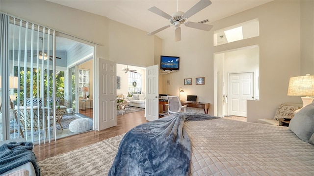 bedroom with access to exterior, hardwood / wood-style flooring, ceiling fan, and a high ceiling