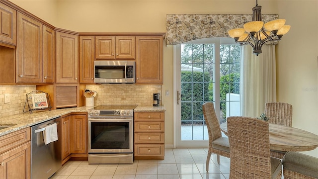 kitchen with appliances with stainless steel finishes, pendant lighting, backsplash, light tile patterned floors, and light stone counters