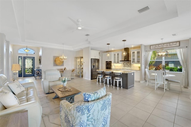 tiled living room with sink, a tray ceiling, ceiling fan with notable chandelier, and french doors