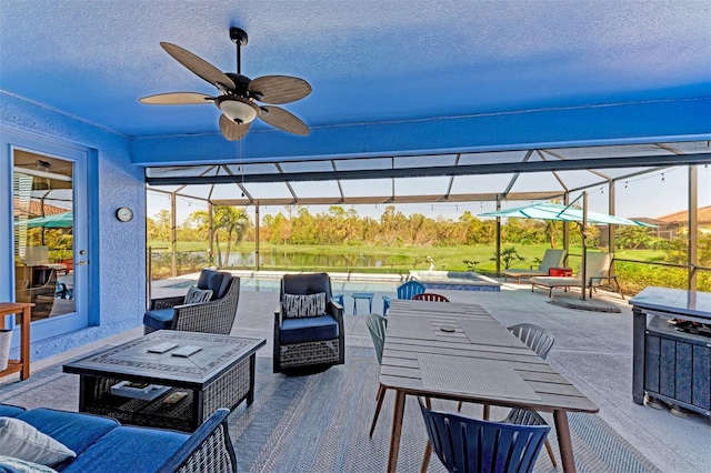 view of patio with a lanai, outdoor lounge area, ceiling fan, and a water view