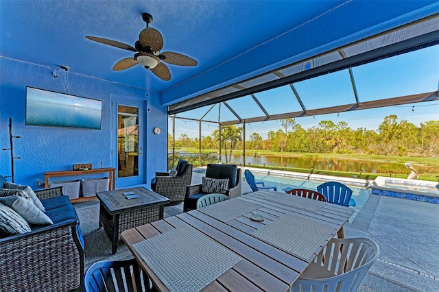 view of patio / terrace with a lanai, an outdoor living space with a fire pit, ceiling fan, and a water view