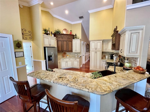 kitchen featuring a kitchen breakfast bar, kitchen peninsula, stainless steel fridge with ice dispenser, and backsplash