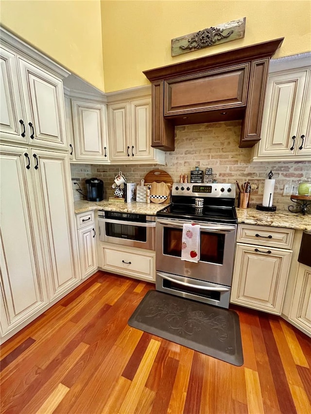 kitchen with cream cabinets, light hardwood / wood-style flooring, electric range, and decorative backsplash