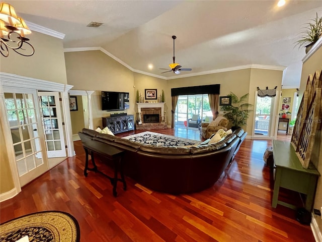 living room featuring lofted ceiling, crown molding, hardwood / wood-style floors, a brick fireplace, and ceiling fan with notable chandelier