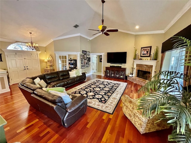 living room featuring a fireplace, ornamental molding, wood-type flooring, ceiling fan with notable chandelier, and vaulted ceiling