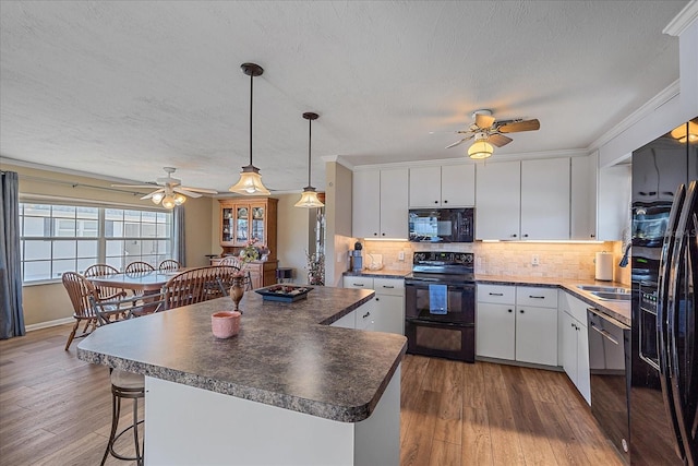 kitchen featuring tasteful backsplash, white cabinets, hanging light fixtures, and black appliances