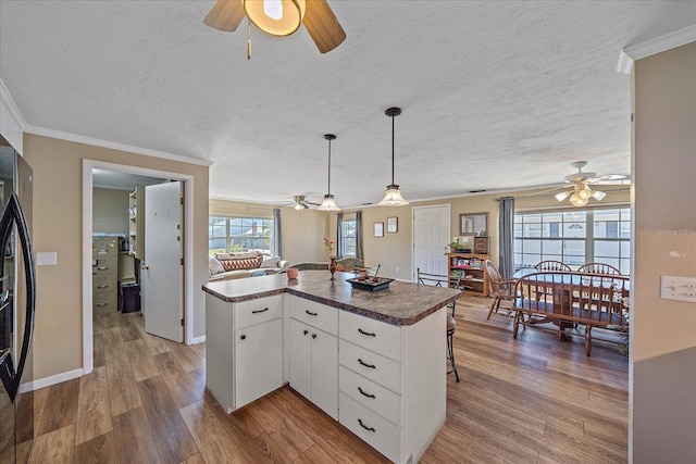 kitchen featuring white cabinetry, hanging light fixtures, wood-type flooring, ornamental molding, and a textured ceiling