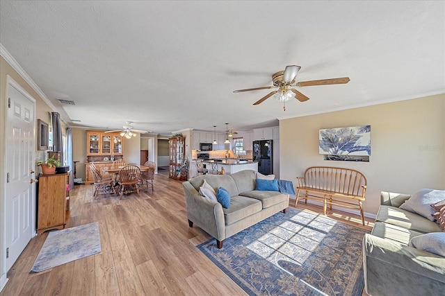 living room featuring crown molding, a textured ceiling, ceiling fan, and light wood-type flooring