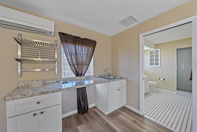 kitchen featuring white cabinetry, sink, a wall mounted AC, and light hardwood / wood-style flooring