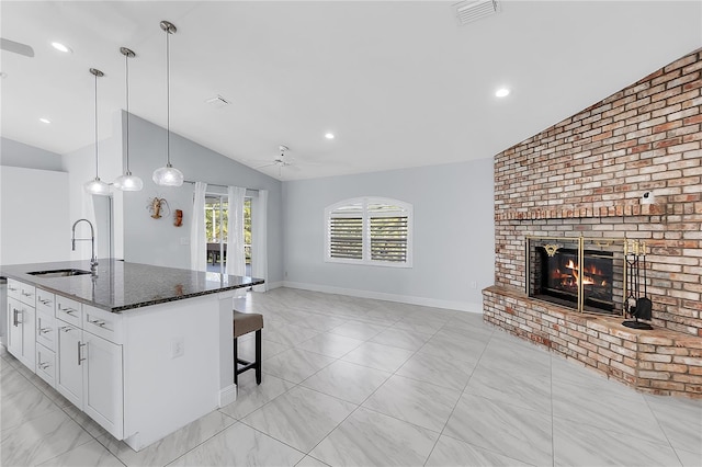 kitchen featuring lofted ceiling, sink, dark stone countertops, white cabinets, and a center island with sink