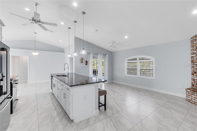 kitchen featuring lofted ceiling, sink, dark stone countertops, a kitchen island with sink, and white cabinets