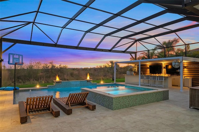 pool at dusk featuring an in ground hot tub, an outdoor kitchen, a lanai, and an outdoor bar