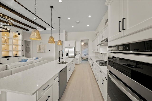 kitchen with sink, white cabinetry, hanging light fixtures, stainless steel appliances, and a large island with sink