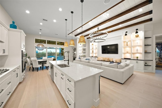 kitchen with pendant lighting, an island with sink, sink, white cabinets, and light stone countertops