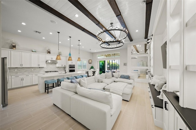 living room featuring beamed ceiling, sink, a notable chandelier, and light wood-type flooring